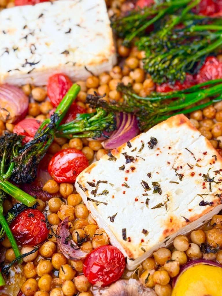 Golden baked feta with chickpeas, tomatoes, red onion, and charred broccolini on a parchment-lined sheet pan