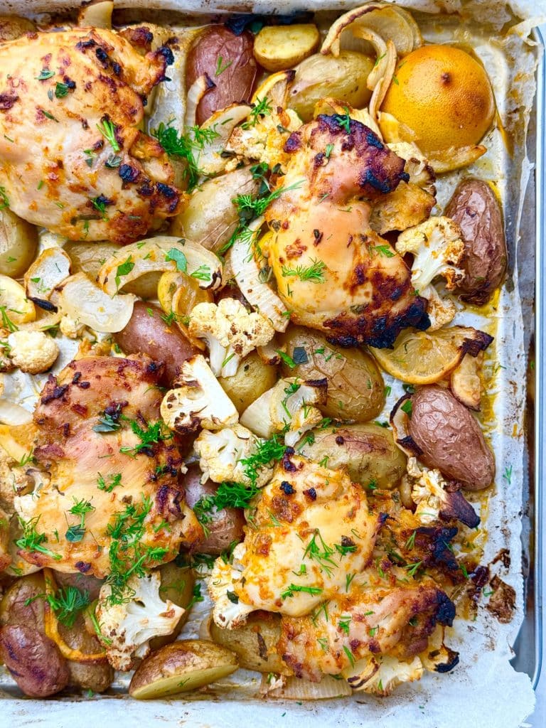 Overhead view of sheet pan chicken and potatoes with lots of lemon, roasted with cauliflower, onion, and fresh herbs.