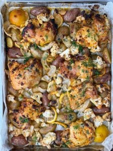 Overhead sheet pan view of chicken and potatoes with cauliflower and lemon slices ready to serve.