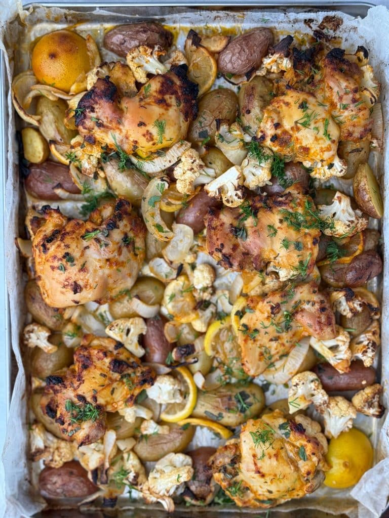 Overhead sheet pan view of chicken and potatoes with cauliflower and lemon slices ready to serve.