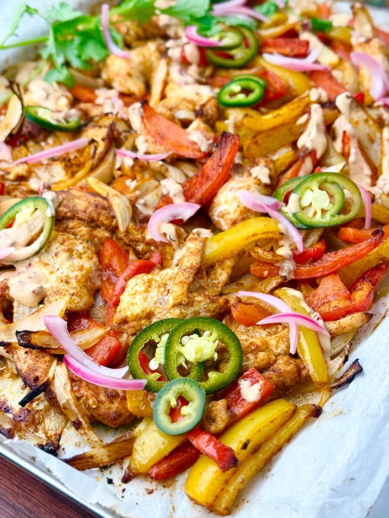 Close-up of chicken fajita tacos filled with roasted peppers, onions, pickled jalapeños, pickled red onions, and cilantro on soft flour tortillas with lime wedges.