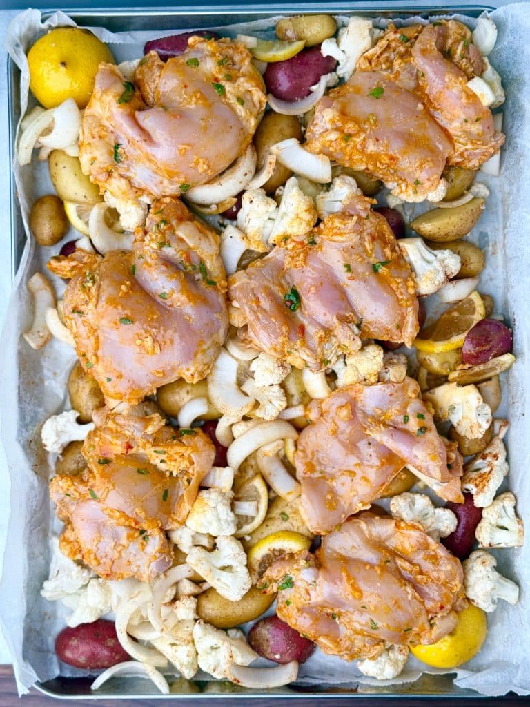 Overhead shot of raw chicken and seasoned vegetables arranged on a sheet pan before roasting.
