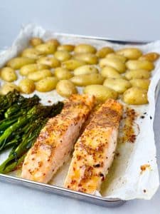 Angled shot of a sheet pan featuring two cooked honey mustard salmon fillets, roasted broccolini, and crispy baby potatoes.