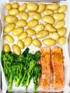 Partially roasted sheet pan with golden potatoes, fresh broccolini, and raw honey mustard-glazed salmon fillets arranged side by side.