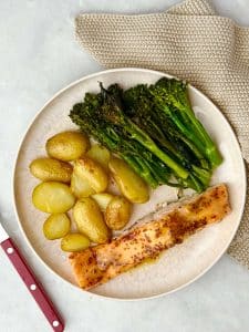 Overhead view of a complete plated meal with roasted baby potatoes, broccolini, and honey mustard salmon, set on a neutral-toned background.