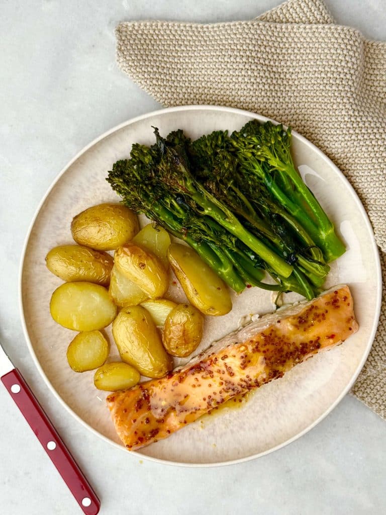 Overhead view of a complete plated meal with roasted baby potatoes, broccolini, and honey mustard salmon, set on a neutral-toned background.