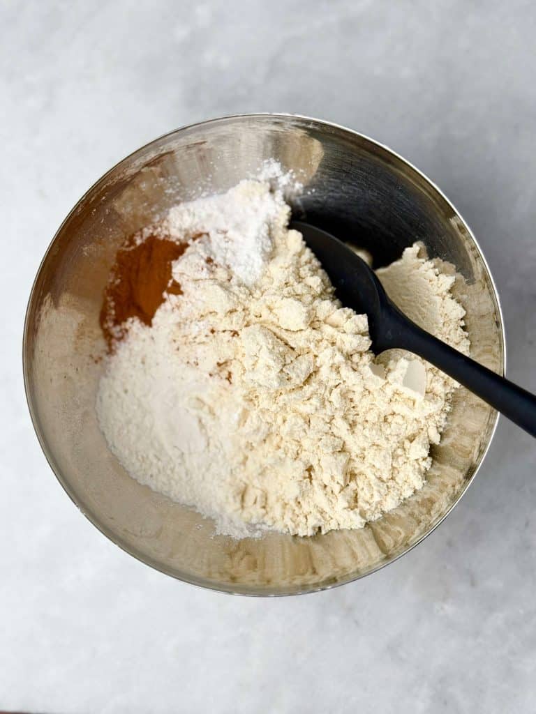 Mixing bowl filled with flour, protein powder, cinnamon, and baking powder for sheet pan banana protein pancakes.