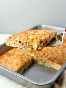 Fluffy sheet pan banana protein pancake slice lifted from baking dish, golden and soft inside.