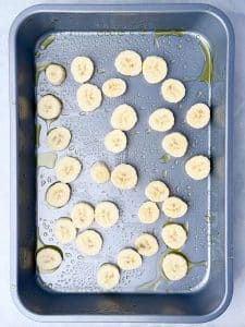 Fresh banana slices arranged in a greased baking dish before adding pancake batter.