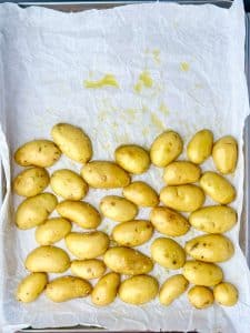 Raw baby potatoes on a parchment-lined sheet pan, tossed with olive oil, salt, and ready for roasting.