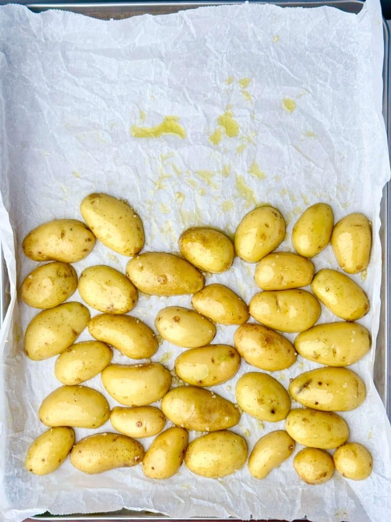 Raw baby potatoes on a parchment-lined sheet pan, tossed with olive oil, salt, and ready for roasting.