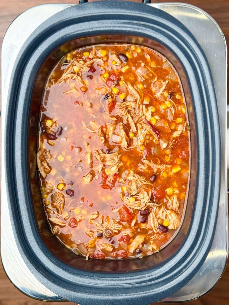 Crockpot filled with simmering chicken tortilla soup made with shredded chicken, black beans, corn, tomatoes, and spices.