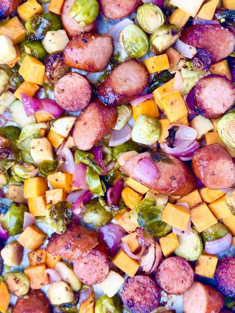 Detailed view of roasted fall sausage and veggie sheet pan with sweet potatoes, Brussels sprouts, and apples.