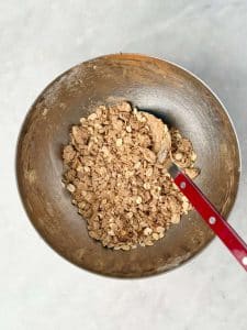 Apple crisp with protein powder crumble topping, baked in red ramekins, shown close-up with golden oats.