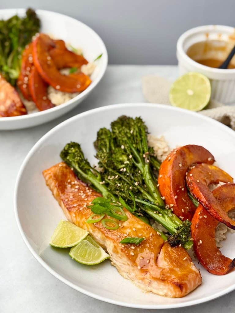 Sheet pan miso salmon served with roasted kabocha, broccolini, and rice in a white bowl, with lime wedges and sauce ramekin in the background