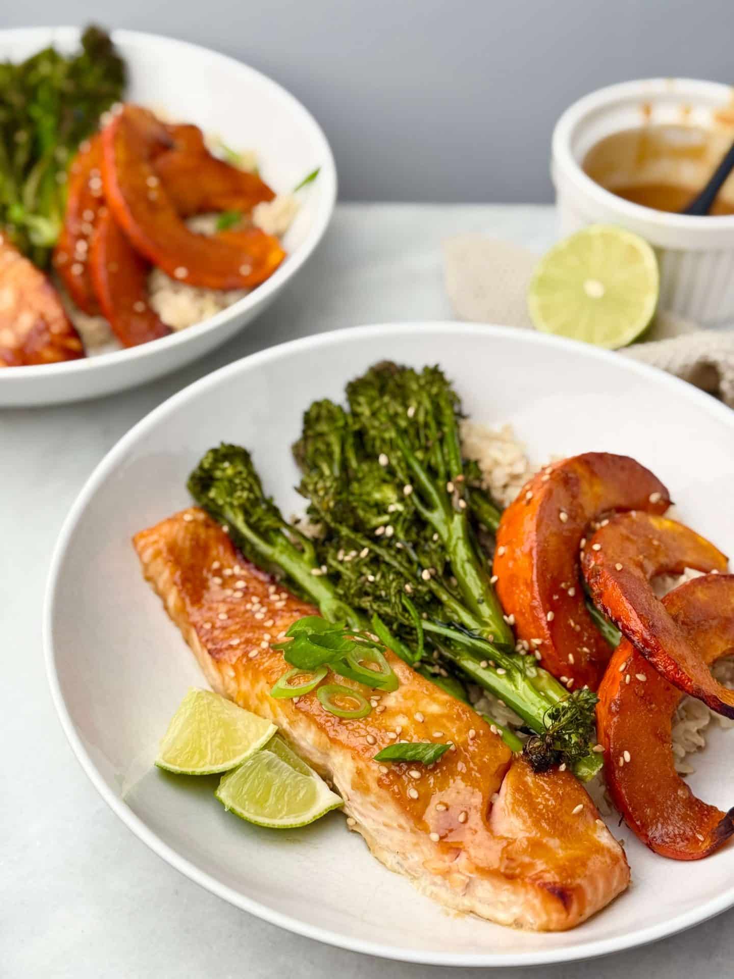Sheet pan miso salmon served with roasted kabocha, broccolini, and rice in a white bowl, with lime wedges and sauce ramekin in the background