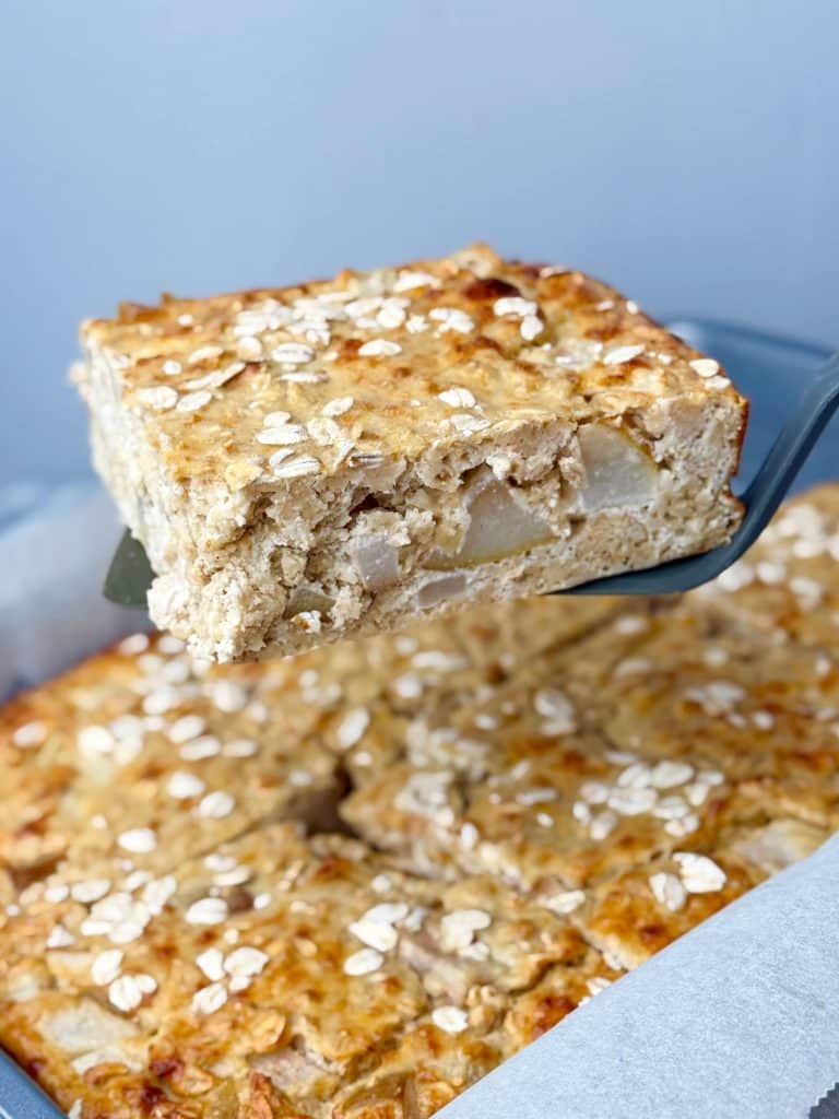 Tray of pear cardamom baked oat bars with one square lifted out on a spatula.