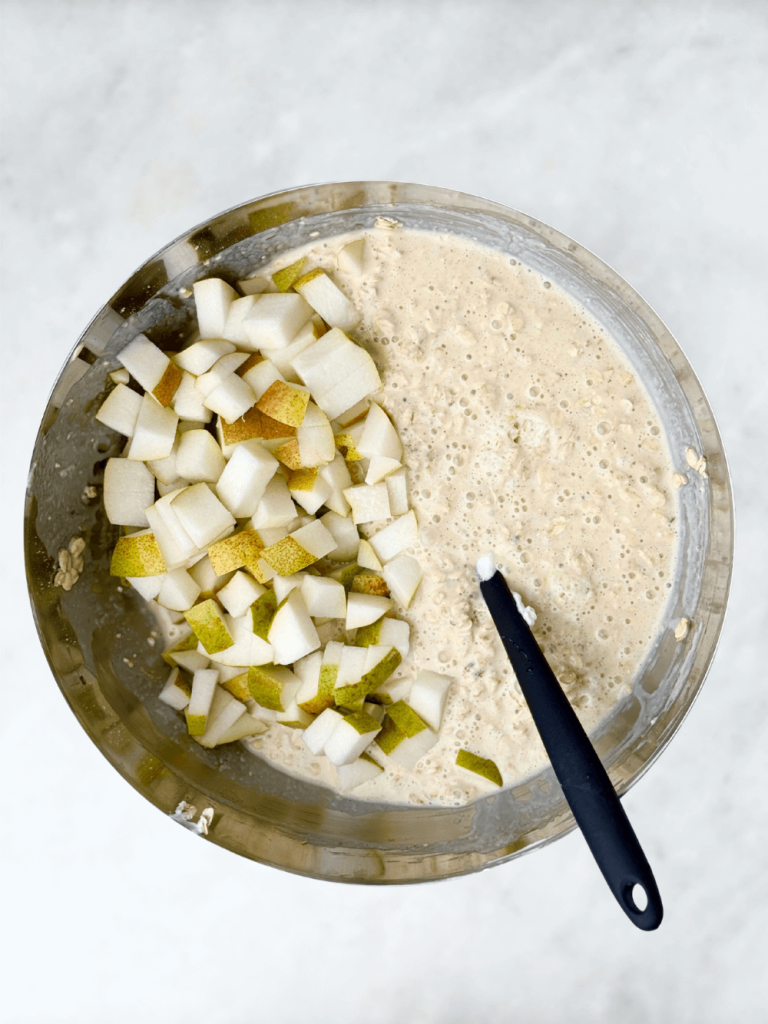 Diced fresh pears folded into oat batter in a large mixing bowl.