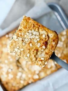 Close-up of a single pear cardamom baked oat bar slice on a spatula, showing golden oat topping.