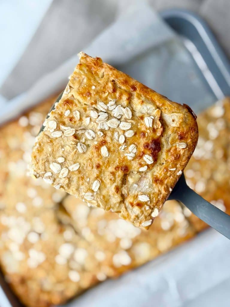 Close-up of a single pear cardamom baked oat bar slice on a spatula, showing golden oat topping.