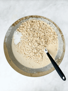Rolled oats added into the wet batter mixture in a large mixing bowl.