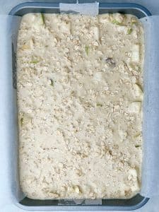 Unbaked pear cardamom oat mixture spread in a tray and sprinkled with oats before baking.