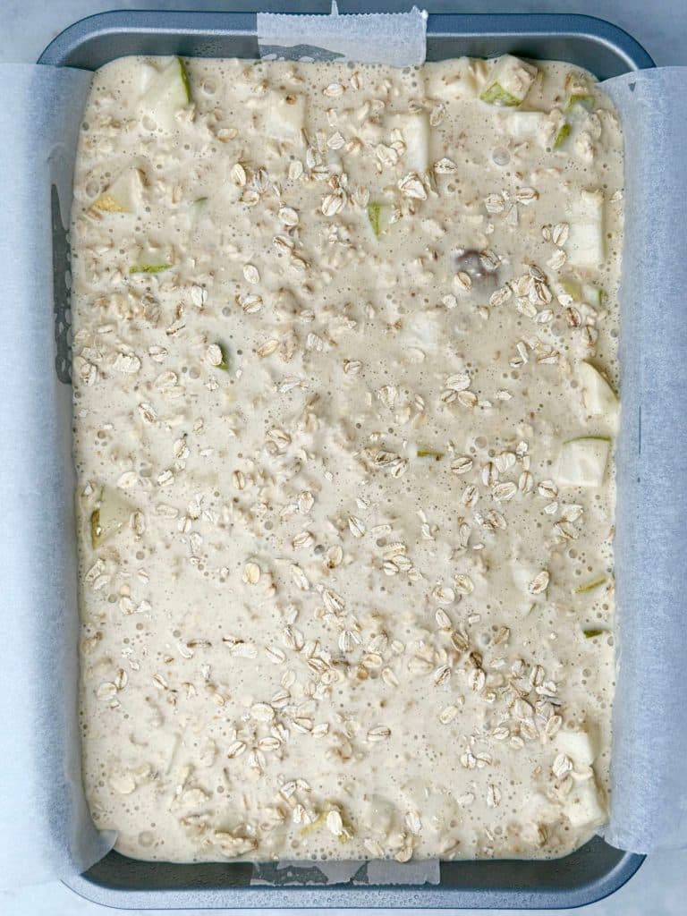 Unbaked pear cardamom oat mixture spread in a tray and sprinkled with oats before baking.