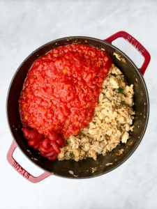 A Dutch oven filled with browned chicken mixture and fresh tomatoes with tomato paste before stirring.
