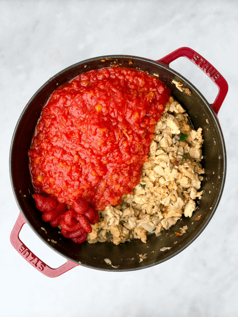 A Dutch oven filled with browned chicken mixture and fresh tomatoes with tomato paste before stirring.