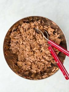 Shredded beef in bowl with forks after slow cooking for crockpot birria soup.