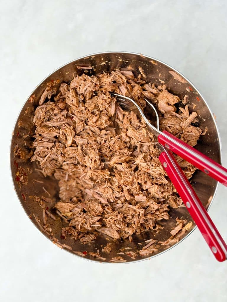 Shredded beef in bowl with forks after slow cooking for crockpot birria soup.