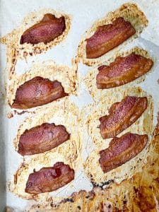 Crispy baked thick-cut bacon cooling on a parchment-lined sheet pan.