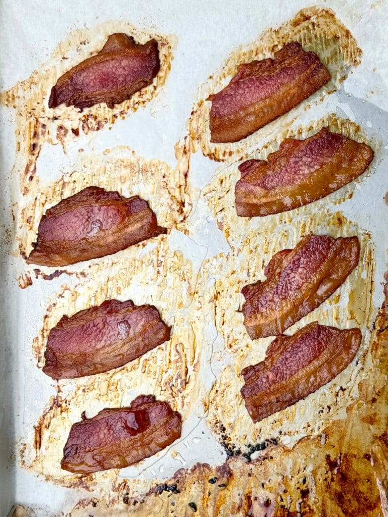 Crispy baked thick-cut bacon cooling on a parchment-lined sheet pan.