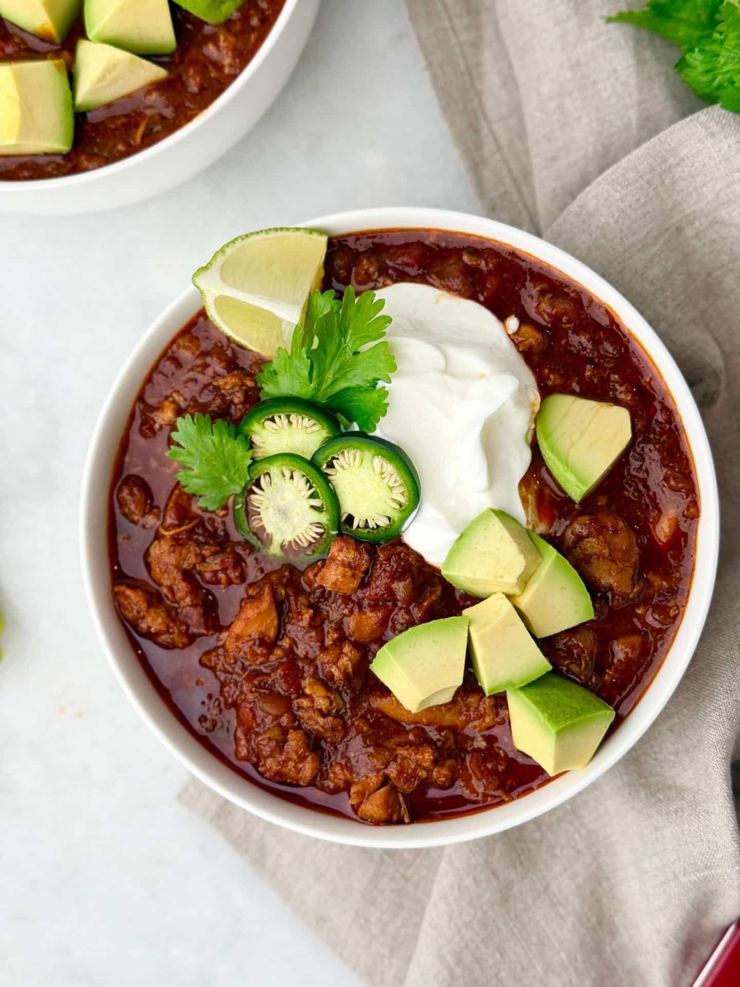 Overhead view of a bowl of chicken chili with avocado, jalapeño, lime, cilantro, and Greek yogurt on top.