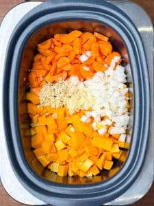 Chopped butternut squash, onion, carrots, garlic, and ginger layered in a crockpot for curry base.