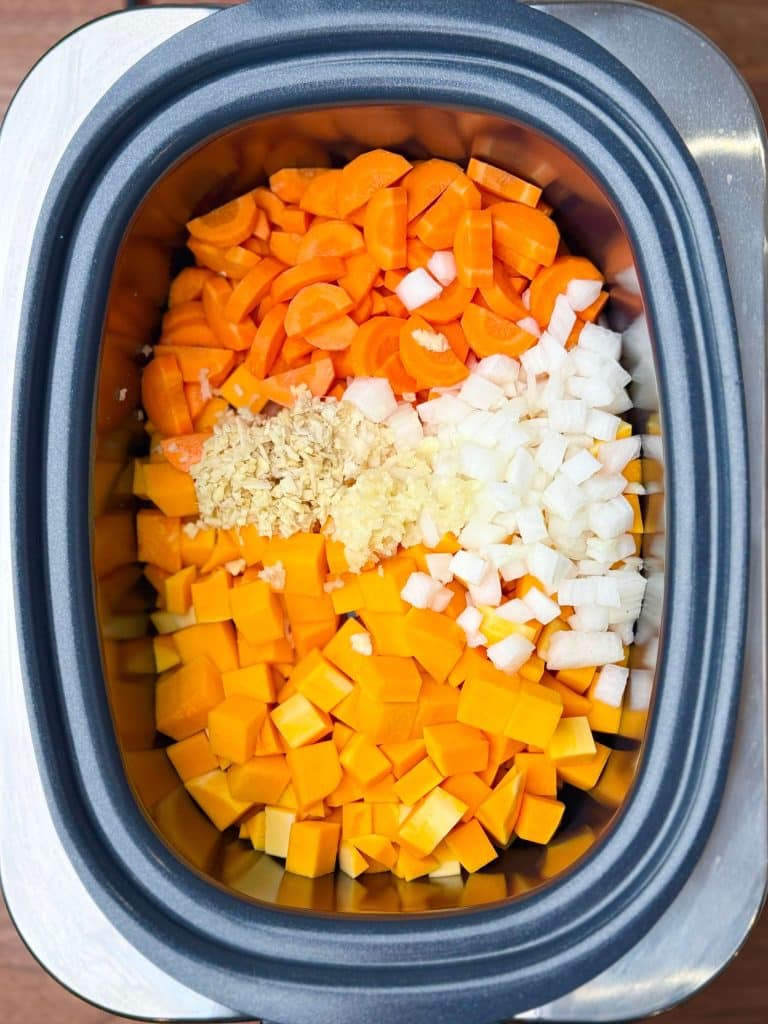 Chopped butternut squash, onion, carrots, garlic, and ginger layered in a crockpot for curry base.