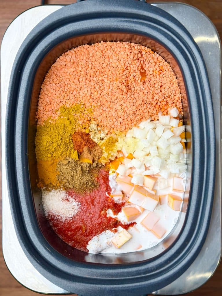 Red lentils, curry spices, coconut milk, and crushed tomatoes added to vegetables in crockpot for butternut squash curry.
