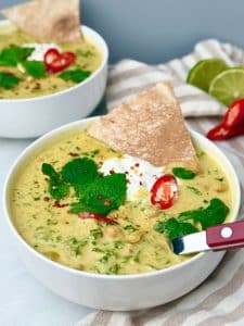 Crockpot spiced chickpea stew with coconut milk, greens, yogurt, fresh herbs, and pita, served in a white bowl.