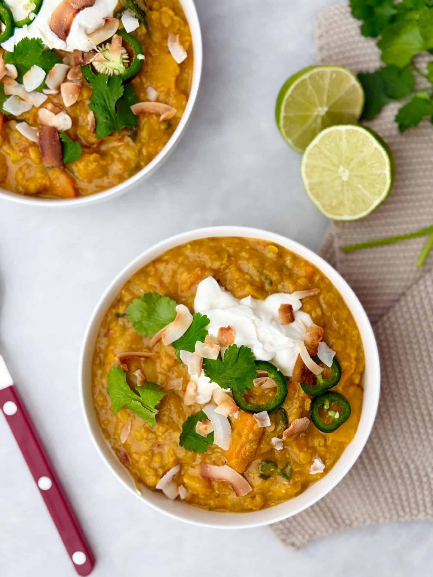 Two bowls of crockpot butternut squash and red lentil curry topped with yogurt, jalapeños, toasted coconut, and cilantro.