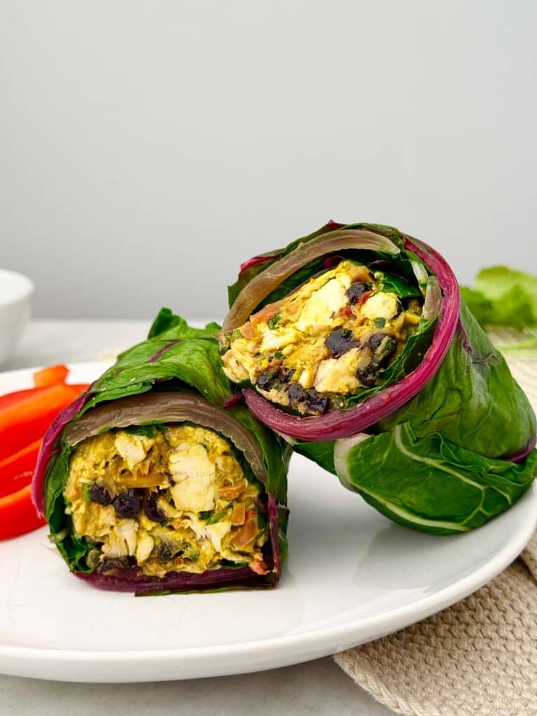 Collard green wrap filled with curry chicken salad, sliced in half to show creamy chicken, blueberries, and almonds inside.