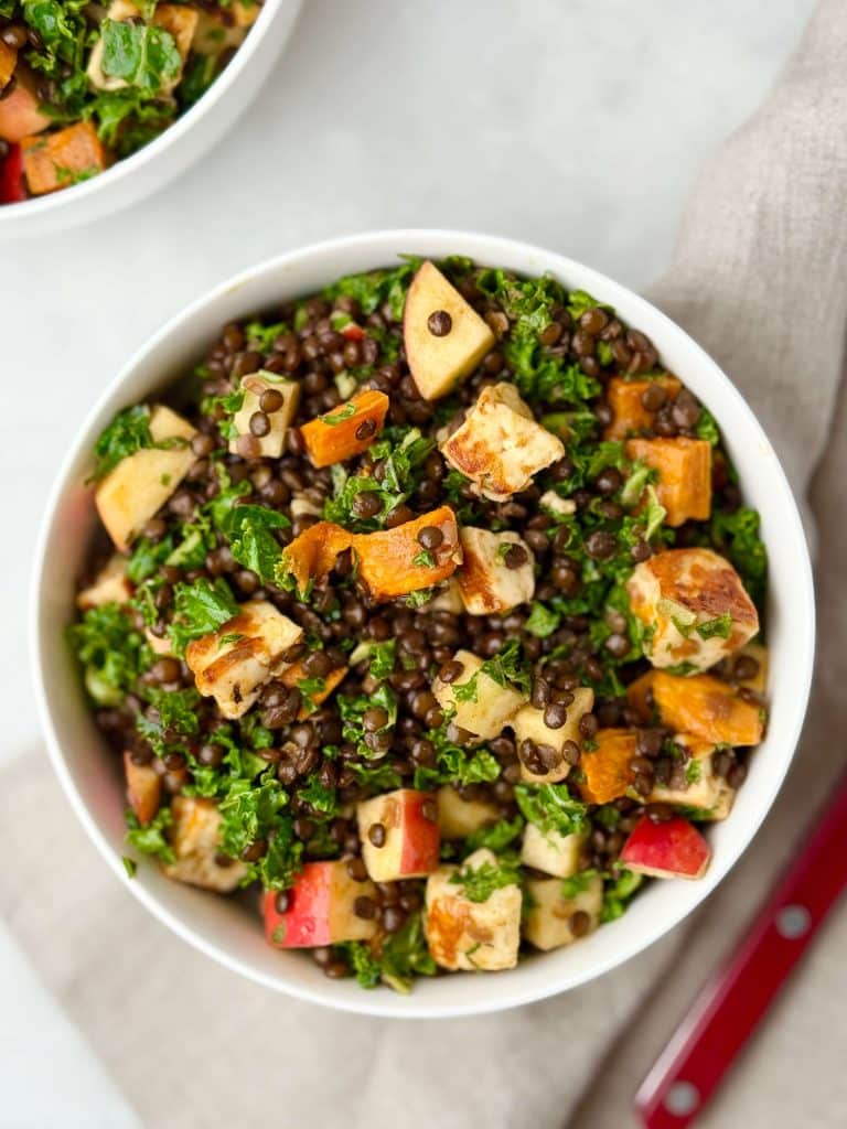 Bowl of fall lentil salad recipe with roasted sweet potatoes, apples, kale, black lentils, and crispy halloumi.