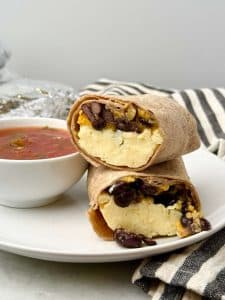 High protein freezer breakfast burrito cut in half on a white plate, filled with fluffy scrambled eggs, black beans, and melted cheddar, served with salsa.