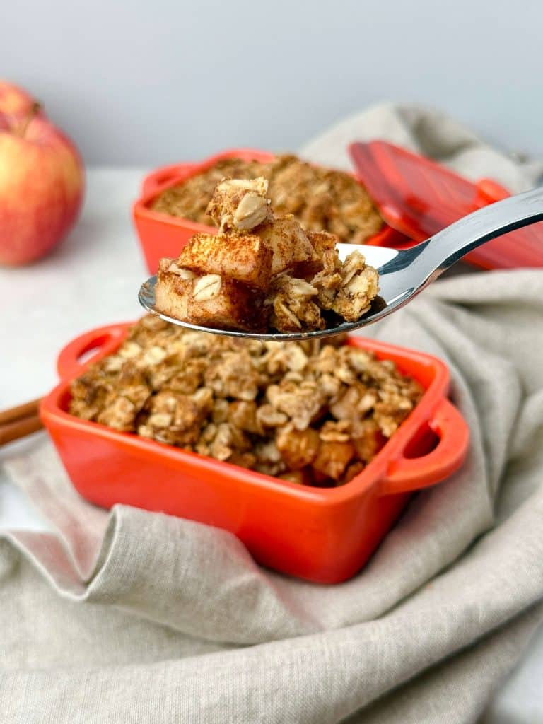 Healthy apple crisp served in a red baking dish with a spoonful showing tender cinnamon apples and oat topping.