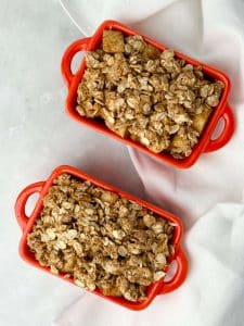 Healthy apple crisp recipe baked in red ramekins, topped with creamy Greek yogurt on a linen cloth.