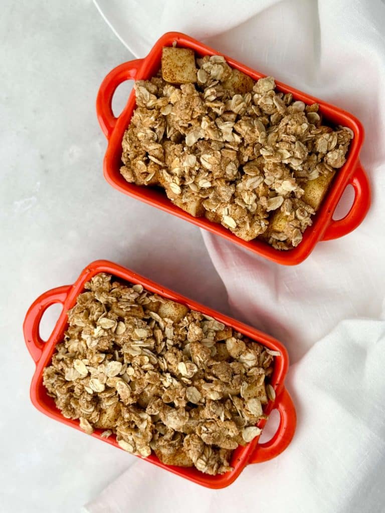 Healthy apple crisp recipe baked in red ramekins, topped with creamy Greek yogurt on a linen cloth.