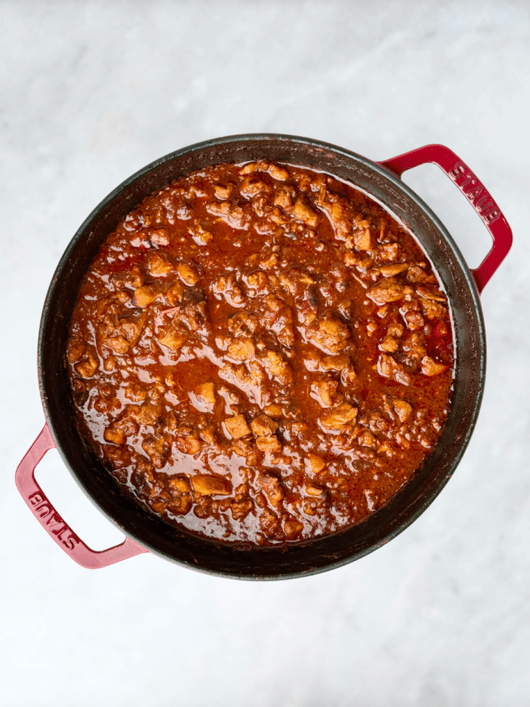 A large red Dutch oven filled with simmering healthy chicken chili.