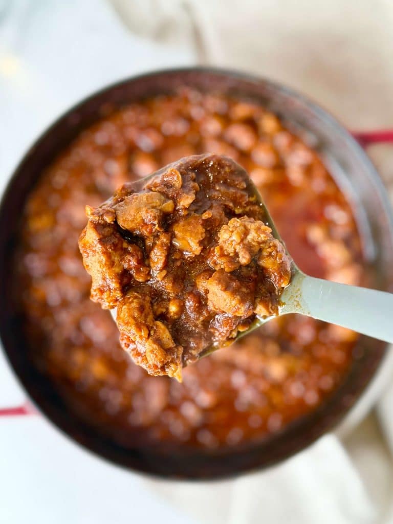 A close-up of a ladle lifting hearty chicken chili from the pot.