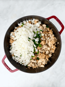 Chopped onion and diced jalapeños added to browned chicken and sausage in a Dutch oven.