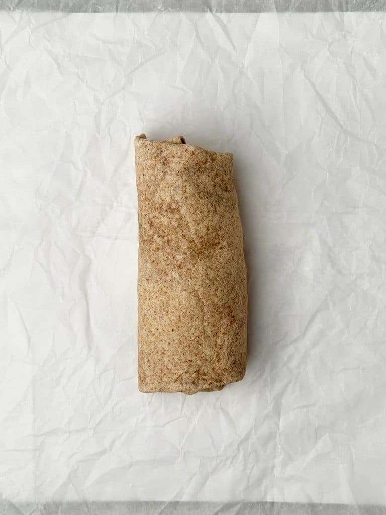 Rolled whole wheat tortilla burrito filled with eggs, beans, and cheese, prepped for freezing.