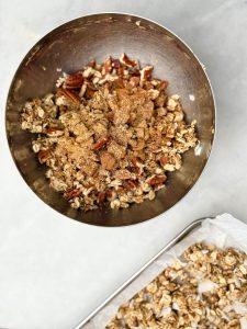 Mixing bowl of oats, chopped pecans, and pumpkin spice being combined to make a high-protein granola flavor variation.